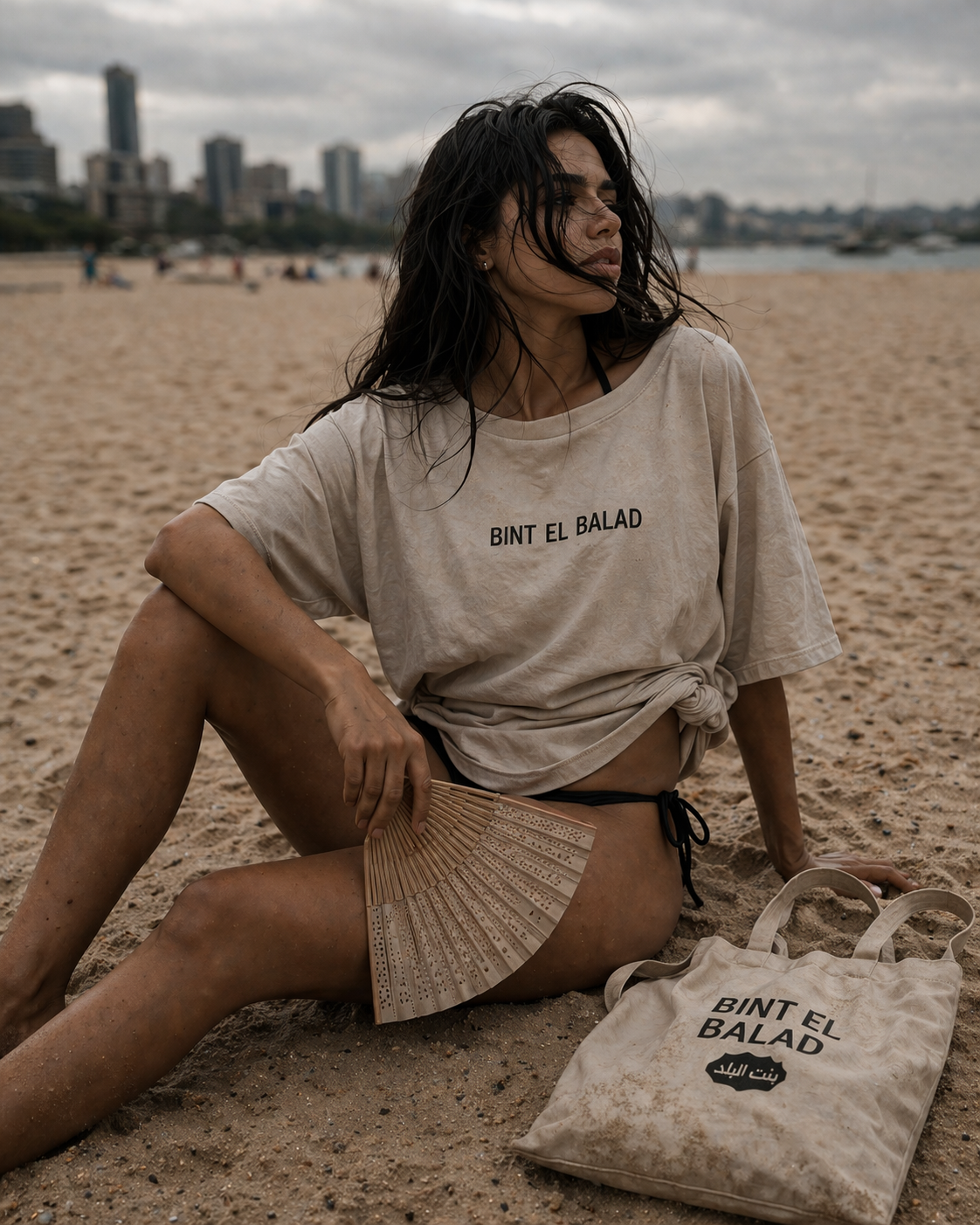 Arab Hyphenated woman sitting on beach with tote and tee 